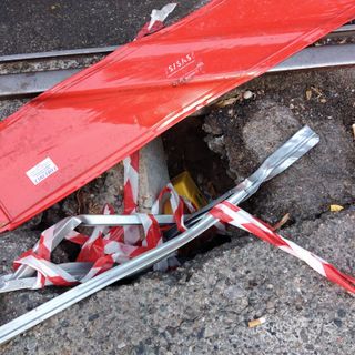 Buco nella strada con binario a poca distanza e transenna