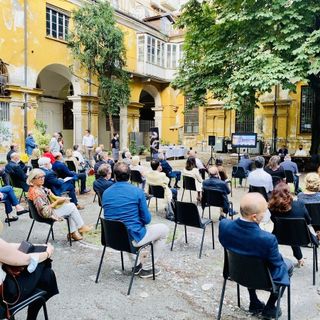 Persone sedute su sedie distanziate in un cortile