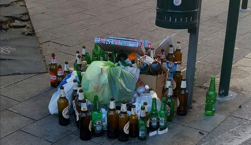 Bottiglie vuote e cartoni della pizza abbandonati vicino a un cestino dei rifiuti