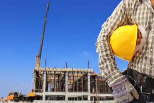 muratore con caschetto sotto il braccio e cantiere sullo sfondo