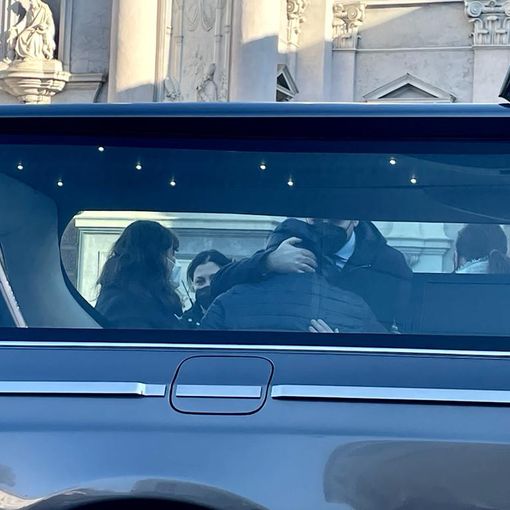 carro funebre e persone che si abbracciano
