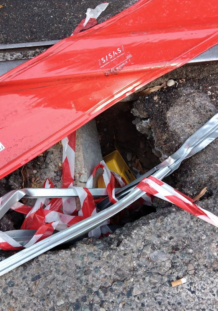 Buco nella strada con binario a poca distanza e transenna