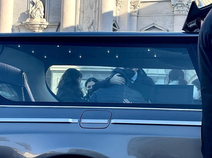 carro funebre e persone che si abbracciano