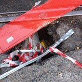 Buco nella strada con binario a poca distanza e transenna