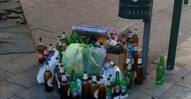 Bottiglie vuote e cartoni della pizza abbandonati vicino a un cestino dei rifiuti